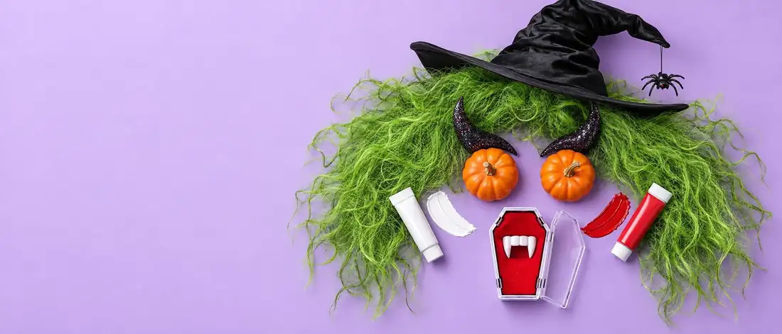 Halloween-asusteista koottu hirviön naama: vihreä peruukki, noitahattu, kurpitsasilmät, pirunsarvet ja vampyyrinhampaat